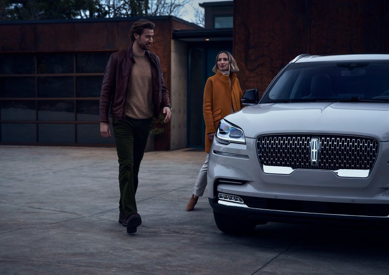 A man and a woman approaching a 2024 Lincoln Aviator® SUV, which illuminates certain lights when they are close | Klaben Lincoln in Kent OH